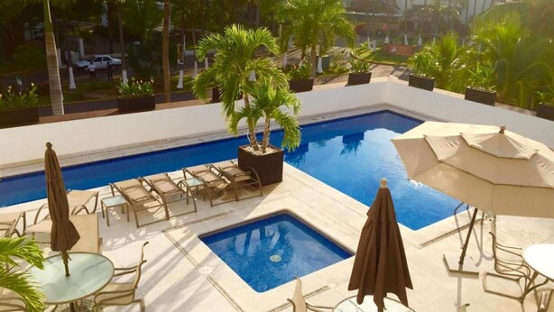 A pool area with lounge chairs and umbrellas, surrounded by potted plants. - Greate apartment at Nuevo Vallarta (Las Jarretaderas)