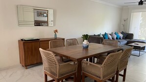 A dining area with a wooden table and wicker chairs, a cabinet, and a sofa in the background. - Greate apartment at Nuevo Vallarta (Las Jarretaderas)