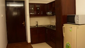 A compact kitchen with dark wooden cabinets, a stainless steel sink, a microwave, and a refrigerator. - MARINERS CABIN LUXURY HOLIDAY APARTMENT  (Nuwara Eliya)
