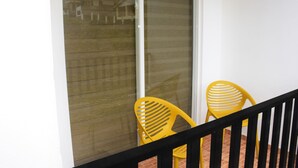 A balcony with a black railing, two yellow chairs, and a sliding glass door. - MARINERS CABIN LUXURY HOLIDAY APARTMENT  (Nuwara Eliya)