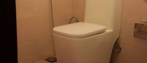 A white toilet with a shower attachment in a bathroom with beige tiles.