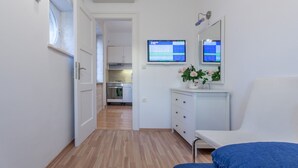 A modern, well-lit room with a wooden floor, a white bed, a small desk with a computer monitor, and a white dresser. - Chic Apartment In Center Of Split (Split)