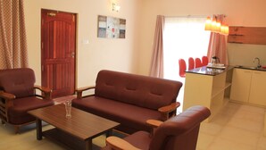 Ein Wohnzimmer mit einer Couch, zwei Sesseln, einem Couchtisch und einer Küchenzeile inklusive Spüle und Arbeitsplatte.