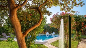 Piscina com cascata, rodeada por um relvado bem cuidado e árvores.