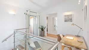 Quarto de hotel moderno com guarda-corrimão de vidro, escrivaninha de madeira, planta em vaso e quadro na parede.