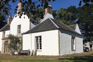 Un bâtiment blanc avec un toit à pignon, une cheminée et un petit porche doté d’un banc.