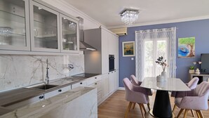 Ett modernt kök med bänkskivor i marmor, en inbyggd diskho och en matplats med ett runt bord och lila stolar.