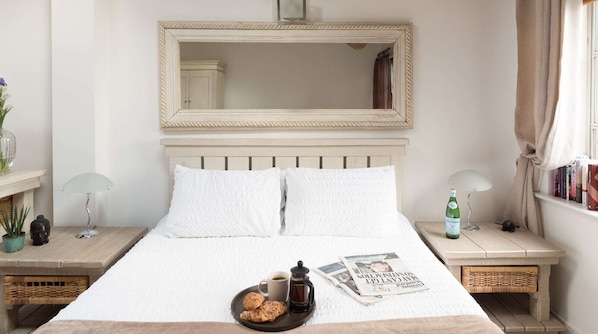 Une chambre à coucher bien rangée, avec un grand lit, deux tables de chevet, un miroir et une fenêtre avec des rideaux.