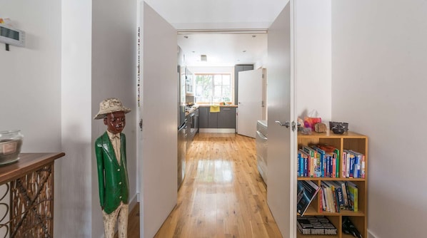 Un couloir doté d’un plancher en bois, d’une bibliothèque remplie de livres et d’une porte donnant sur un espace cuisine.