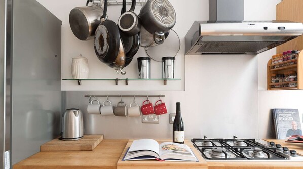 A kitchen with hanging pots, a coffee machine, a kettle, mugs, a wine bottle, and a book on the counter.