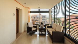 A modern living room with a sofa, two armchairs, a coffee table, and a decorative vase. Large windows with blinds provide a view of the cityscape. - Vilamoura Luxurious PENTHOUSE. 2 large pools, covered parking. (Vilamoura Portugal)