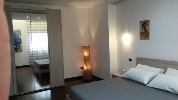 Una habitación de hotel moderna con una cama, una mesita de noche, una lámpara de pared y un cuadro.