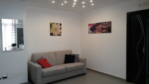 Una sala de estar moderna con un sofá gris, dos cojines, una almohada roja y dos obras de arte colgadas en la pared.