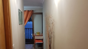 A hallway with wooden flooring, a door on the left, a table with chairs in the background, and a tall vase with branches on the right. - Playa Chica Apartment (SANTA CRUZ DE TENERIFE)