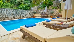 Un espace aménagé au bord de la piscine, avec des chaises longues, une table et un mur en pierre.
