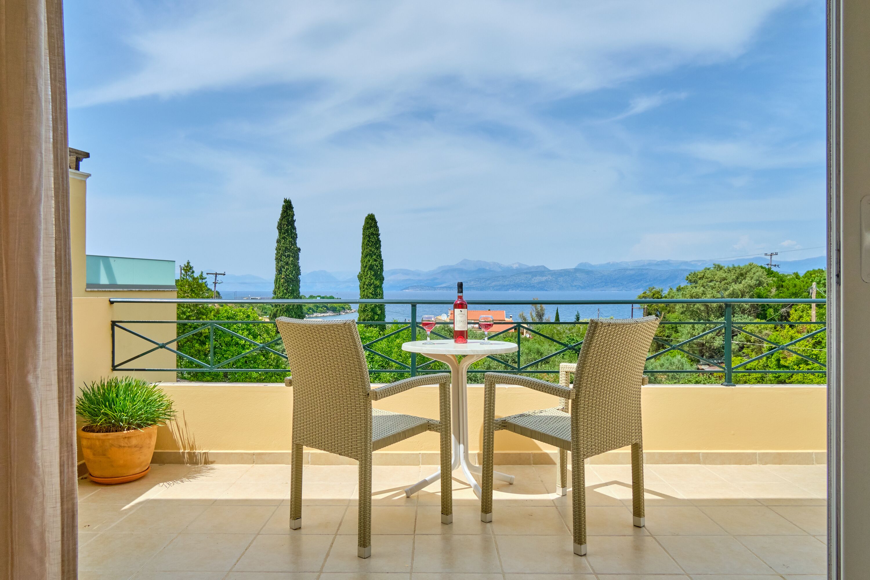 A balcony with two wicker chairs and a small table, overlooking a scenic view of mountains and greenery.