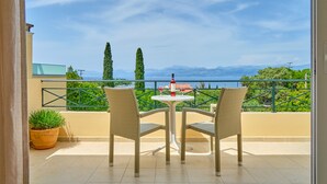 Un balcon avec deux fauteuils en osier et une petite table, offrant une vue panoramique sur les montagnes et la verdure.