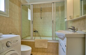 Ein Badezimmer mit Duschkabine, Toilette, Waschmaschine und Waschbecken.