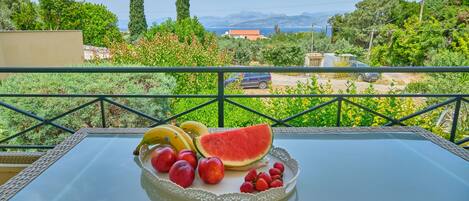 A table with a fruit platter on a balcony overlooking a scenic landscape.