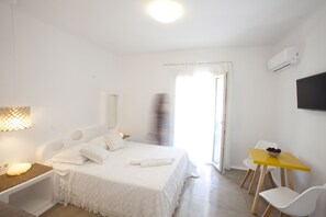 A bedroom with a bed, bedside table, lamp, and a small table with a bowl of fruit.