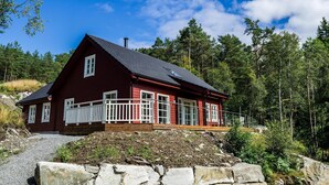 A red wooden house with a white balcony, surrounded by trees and a clear sky. - New, large family friendly cottage, with great views, in rural surroundings (Fusa)