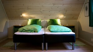A room with two beds, each with green striped pillows and a white mattress. The room has wooden ceiling beams and a green wall. - New, large family friendly cottage, with great views, in rural surroundings (Fusa)