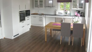 A modern kitchen with white cabinetry, a built-in oven, and a dining area with a wooden table and chairs. - New, large family friendly cottage, with great views, in rural surroundings (Fusa)