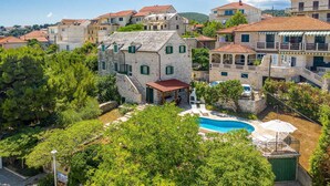 A stone building with a pool and outdoor seating, surrounded by greenery and other buildings. - Traditional Villa Bonaca in Sumartin with private pool, Brač Island, near sea (Sumartin)