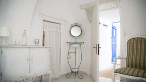 A room with a white cabinet, a small table with a mirror, a chair, and a door leading to another room. - Authentic Trullo with swimming pool in Itria Valley Apulia (Martina Franca)