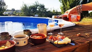 A poolside setting with a table set for a meal, including bowls of chips and a cheese board, a glass of wine, and a bottle being poured. - Authentic Trullo with swimming pool in Itria Valley Apulia (Martina Franca)