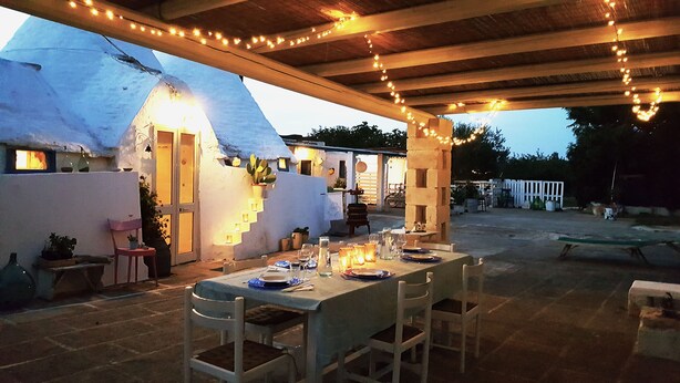 An outdoor dining area with a thatched-roof structure, string lights, and a stone table set for a meal. - Authentic Trullo with swimming pool in Itria Valley Apulia (Martina Franca)