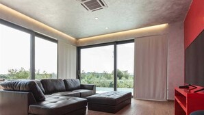 A modern living room with a sectional sofa, a red accent wall, and large windows offering a view of greenery. - Villa Lagoderan Rovinj (Rovinj)