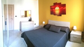 A bedroom with a bed, bedside tables, a dresser, a mirror, and a wall-mounted artwork.