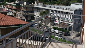 A balcony with a tiled floor and metal railing overlooking a parking area and buildings.