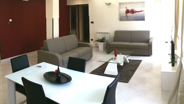 A modern living room with a dining area, a grey sofa, a glass coffee table, and a red abstract painting on the wall.