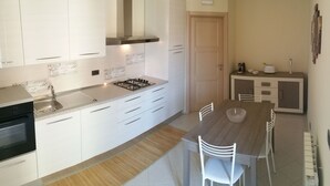 A modern kitchen with white cabinets, a gas stove, and a dining area with a wooden table and white chairs.