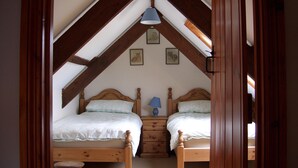 Un dormitorio con dos camas de madera, una mesita de noche y un taburete pequeño.