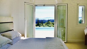 A bedroom with a bed, a window, and a view of a beach and mountains.