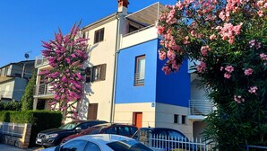 A residential building with balconies, parked cars, and flowering trees.