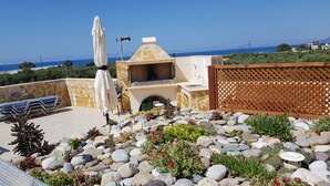 Eine Terrasse mit Steinmauer, Sitzgelegenheiten im Freien, einem Grillplatz und Meerblick.