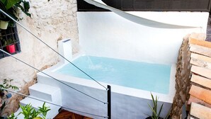 Un petit jacuzzi extérieur avec un mur blanc et une clôture noire en arrière-plan.