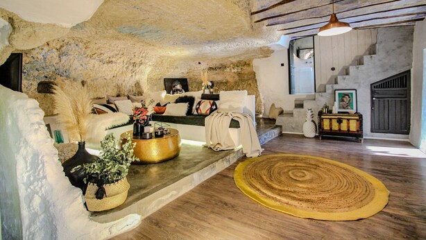 Un intérieur rustique avec des murs en pierre apparentes, un plancher en bois, un canapé, une table basse et un escalier.