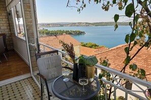 Un balcon avec une table, deux chaises et une vue sur un lac et la ville au loin.