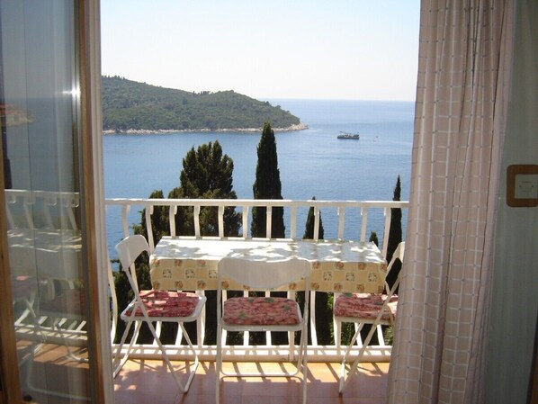 Un balcon avec une table et des chaises, donnant sur une étendue d’eau et une île lointaine.