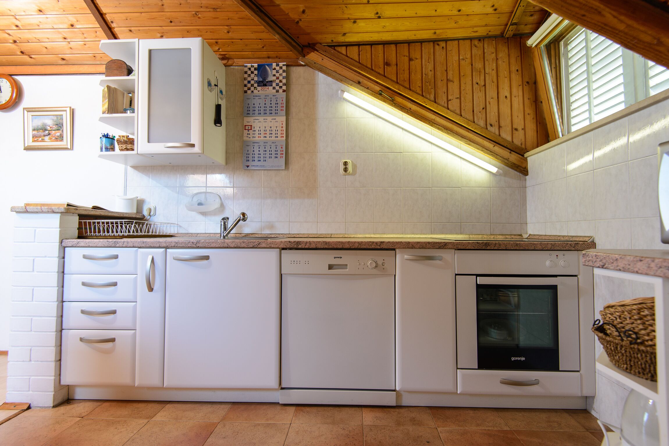 A kitchen with white cabinetry, a dishwasher, an oven, and a window with wooden shutters.
