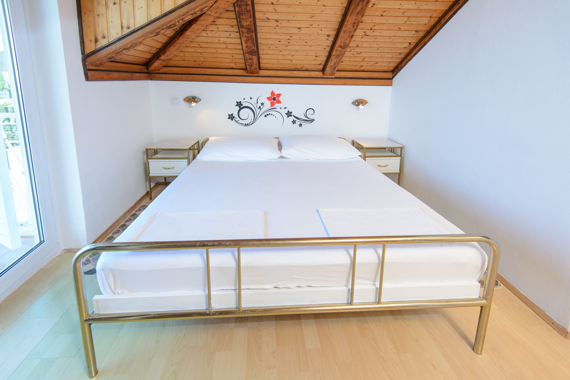 A bed with a metal frame and white bedding in a room with wooden ceiling beams and a decorative wall sticker.