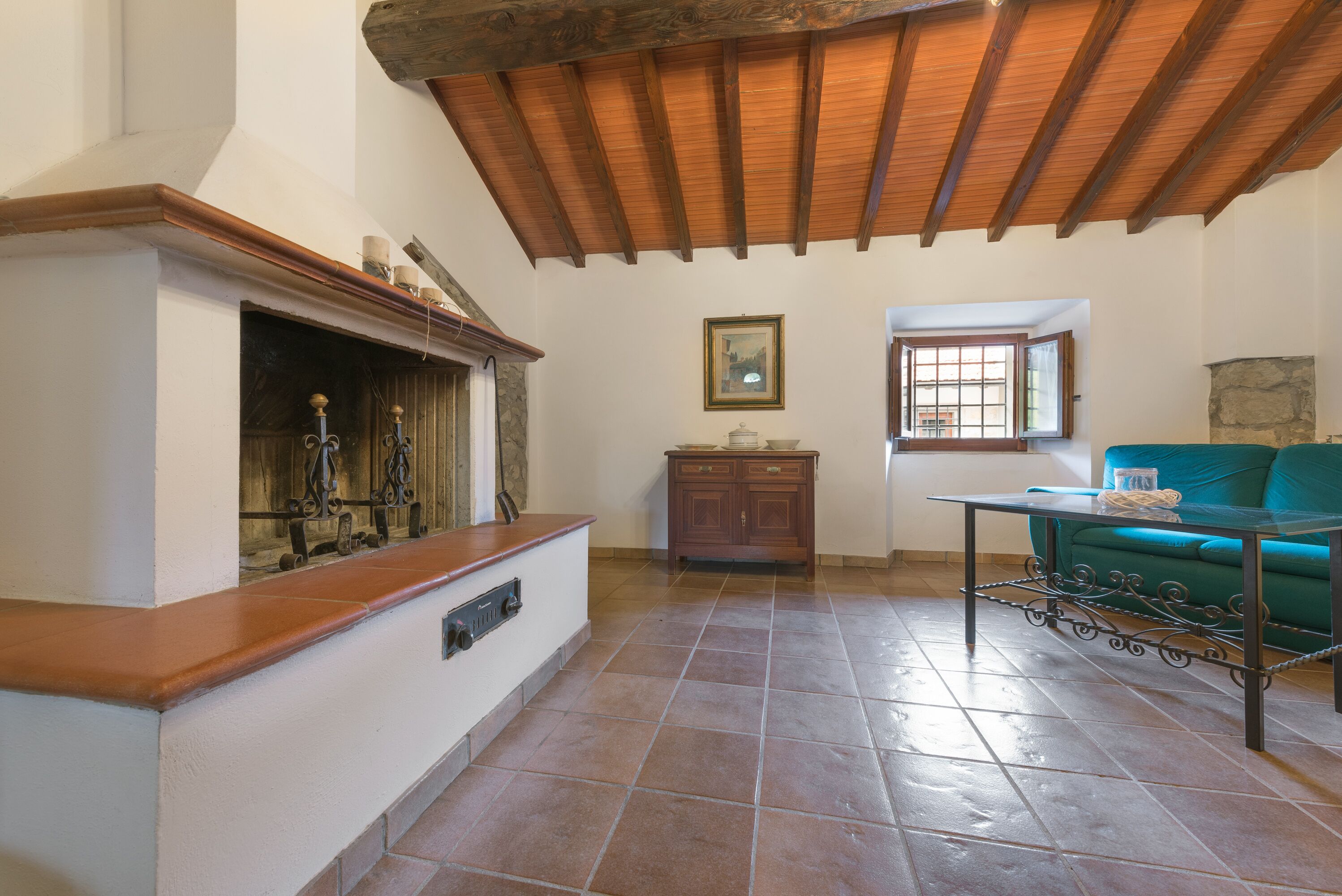 A spacious living room with a wooden ceiling, a stone fireplace, a green sofa, and a tiled floor.