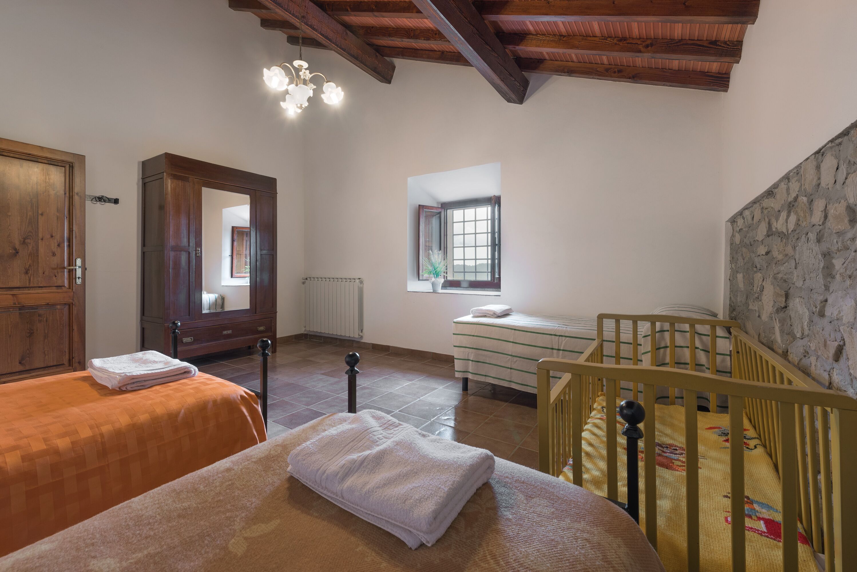 A room with two beds, a crib, a wooden wardrobe, a mirror, and a window.