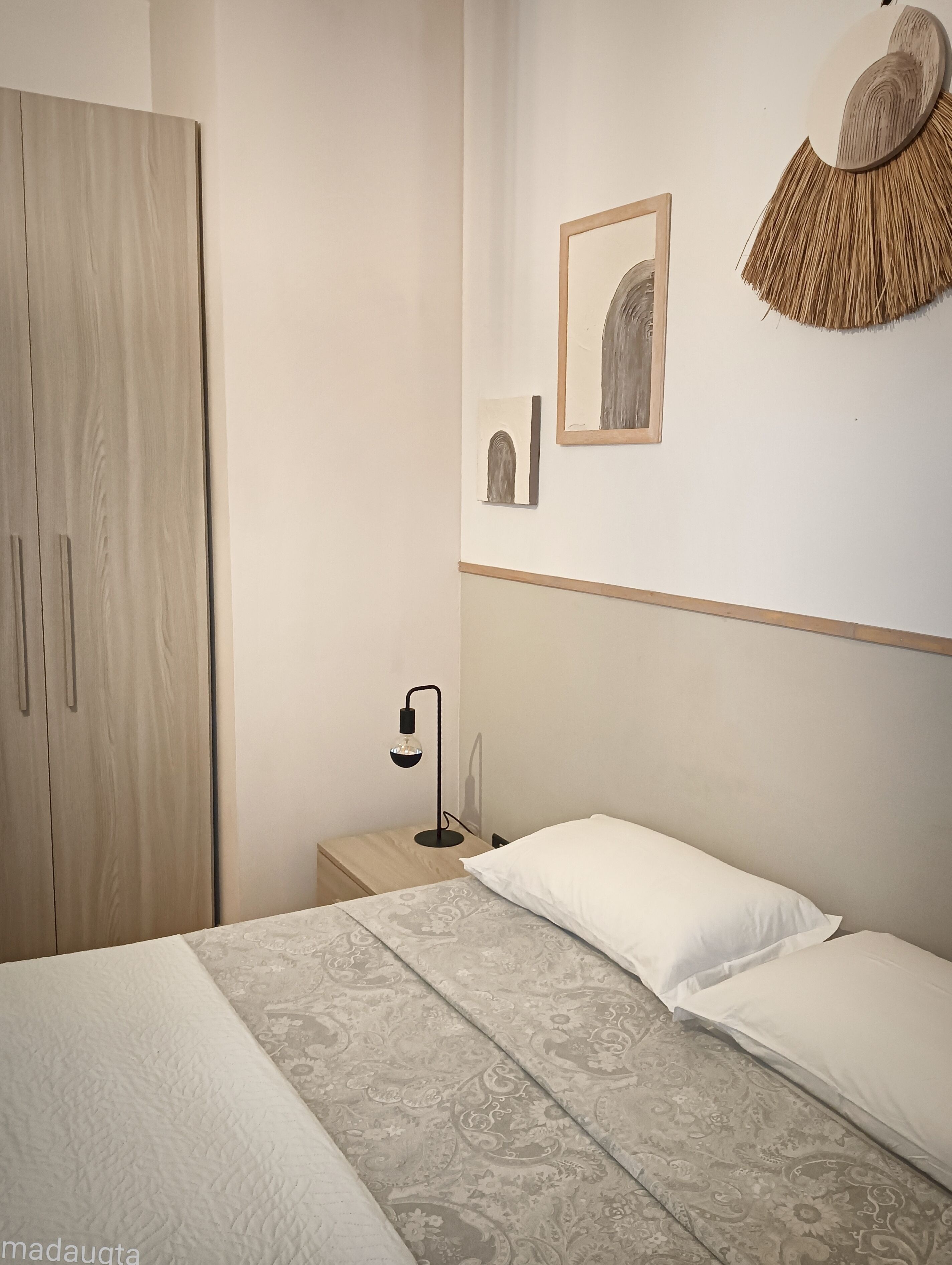 Ein Schlafzimmer mit einem Bett, einem Nachttisch, einer Lampe, einem Kleiderschrank und Wandbildern.