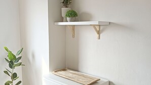 Una habitación de esquina con un tocador blanco, un pequeño estante de madera con una planta, y una planta en maceta al lado del tocador.